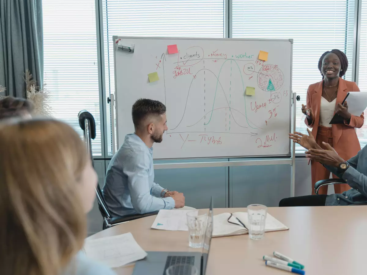 A woman standing in front of a whiteboard, presenting to a group of people.